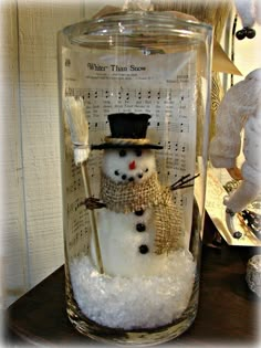 a snowman in a top hat and scarf under a glass jar filled with snow