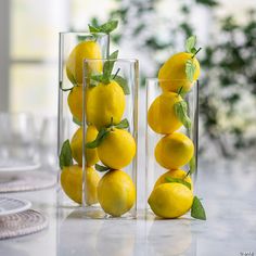 three clear vases filled with lemons on top of a table