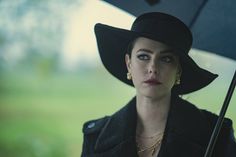 a woman wearing a black hat and holding an umbrella in her hand while looking at the camera