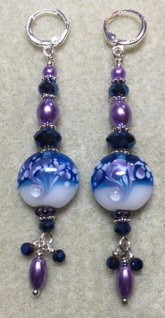 two purple and blue glass beads hanging from silver hoop earrings on a white carpeted surface