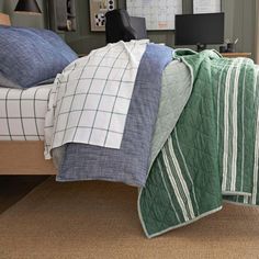 an unmade bed with green and white blankets on it's sides, next to a computer desk