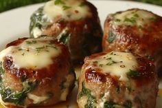 three meatballs covered in cheese and spinach on a plate