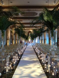 an indoor wedding setup with candles and palm trees in the center, surrounded by clear glass vases