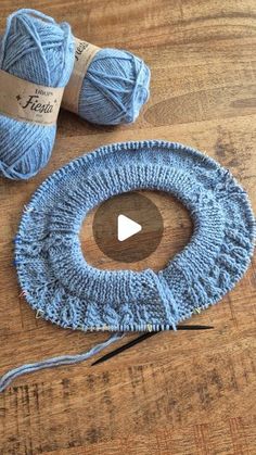 two balls of blue yarn sitting on top of a wooden table next to knitting needles