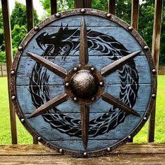 a large metal shield with two dragon heads on it's side, sitting in front of a wooden fence