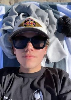 a man wearing sunglasses and a hat laying on top of a blanket