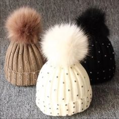 three knit hats with pom - poms sitting on top of a gray carpet