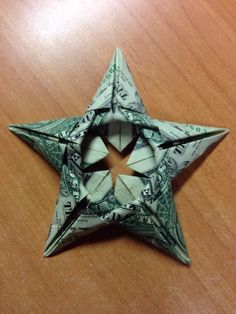 an origami star made out of dollar bills on a wooden table with the center cut out