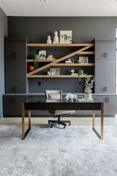 an office with gray walls and shelving units on the wall, along with a black desk