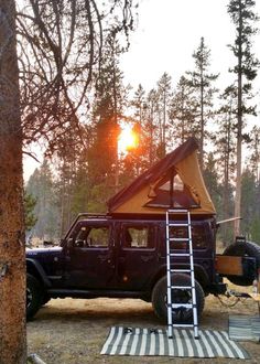 a jeep with a tent on the roof is parked next to a tree and ladder