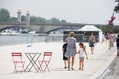 two women and a child walking down the sidewalk near some water with boats in the background