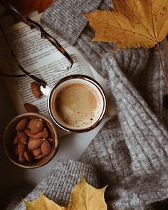 a cup of coffee next to a book and some autumn leaves on a table with a pair of glasses