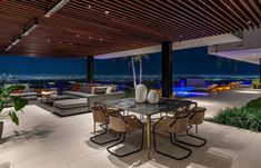 an outdoor living area with couches, tables and chairs in front of a large window at night