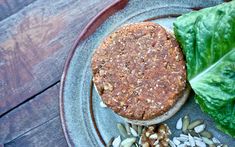 a sandwich on a plate next to lettuce and sunflower seeds, sitting on a wooden table