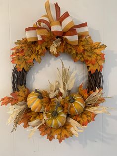 a wreath with fall leaves and pumpkins hanging on a wall