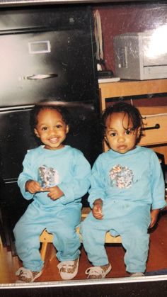 two young children sitting next to each other in front of a dresser and microwave oven