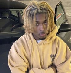 a man with dreadlocks sitting in front of a car