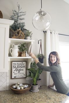 a woman kneeling down next to a potted plant on top of a kitchen counter