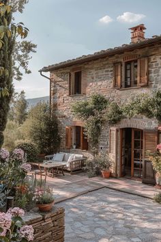 an old stone house with wooden shutters and flowers in the foreground, surrounded by greenery