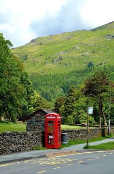 a red phone booth sitting on the side of a road next to a lush green hillside