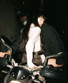 a man and woman riding on the back of a motorcycle at night with helmets on