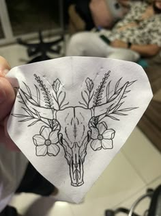 a person holding up a piece of paper with a deer skull and flowers on it