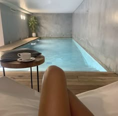 a woman laying in bed next to a swimming pool with a cup of coffee on the side