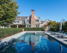 an outdoor swimming pool in front of a large house with trees and lawn chairs around it