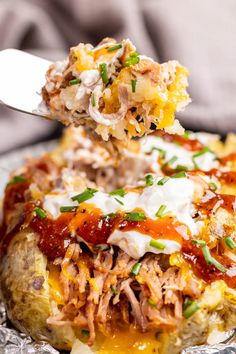 a spoon full of food on top of a baked potato covered in sauce and sour cream