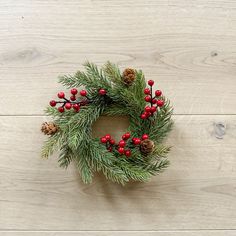 a christmas wreath with red berries and pine cones on a white wooden background, top view