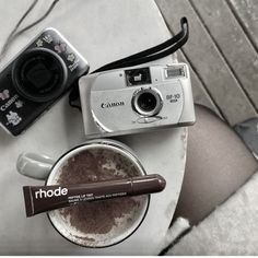 a camera and some other items on a table with a cup of coffee next to it