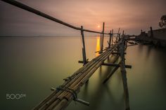 the sun is setting over the water and there are many wooden poles in the water