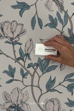 a person is painting a floral wallpaper with blue and white flowers on the wall