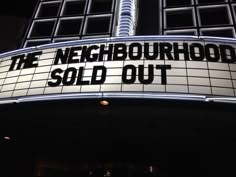 the neighborhood sold out sign is lit up in front of a tall building at night