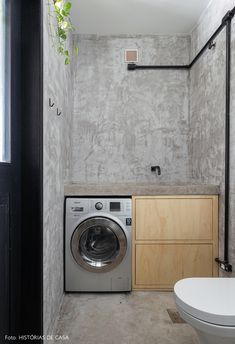 a washer and dryer in a small room with concrete walls, wood cabinets, and a toilet