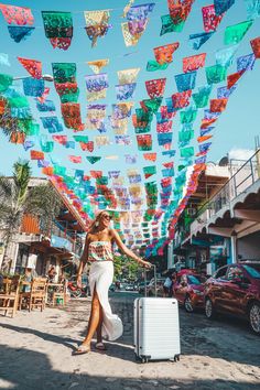 a woman is walking down the street with her luggage and some colorful flags hanging above her