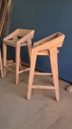 two wooden stools sitting next to each other on the floor in front of a blue wall