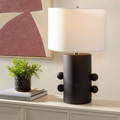 a table lamp sitting on top of a white dresser next to a potted plant