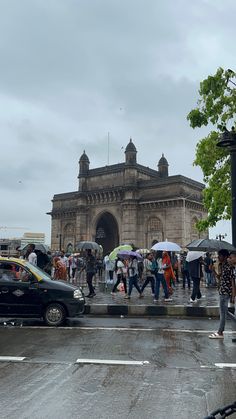 people crossing the street in front of an old building with many arches and windows, while holding umbrellas