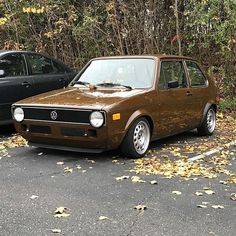 two cars parked next to each other in a parking lot with leaves on the ground