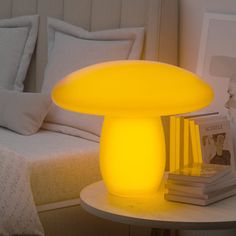 a yellow mushroom lamp sitting on top of a white table next to a bed with pillows