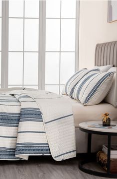 a bed with white and blue striped bedspread next to a window in a bedroom