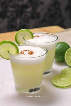 two glasses filled with ice and limes on a table