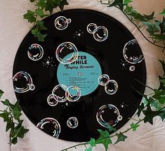 a black record with bubbles on it sitting next to some green leaves and ivys