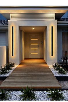 an entrance to a modern house with lights on the front door and wooden steps leading up to it