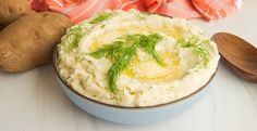 a bowl filled with mashed potatoes and topped with dill garnish next to two wooden spoons