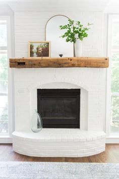 a white brick fireplace in a living room with wood mantel and potted plant