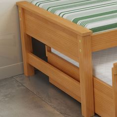 a wooden bed frame with green and white striped bedspread next to a wall