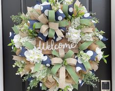 a welcome wreath with flowers and burlocks hanging on the front door for someone to welcome