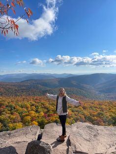 a woman standing on top of a large rock in front of a valley filled with trees